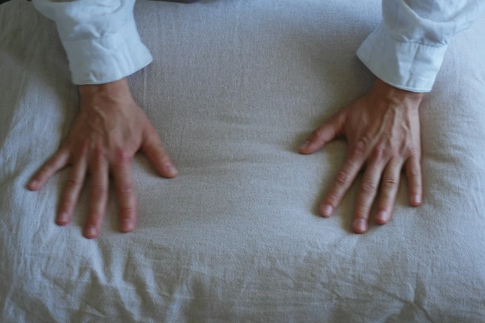 Two hands in white shirt sleeves resting on a textured beige linen pillow